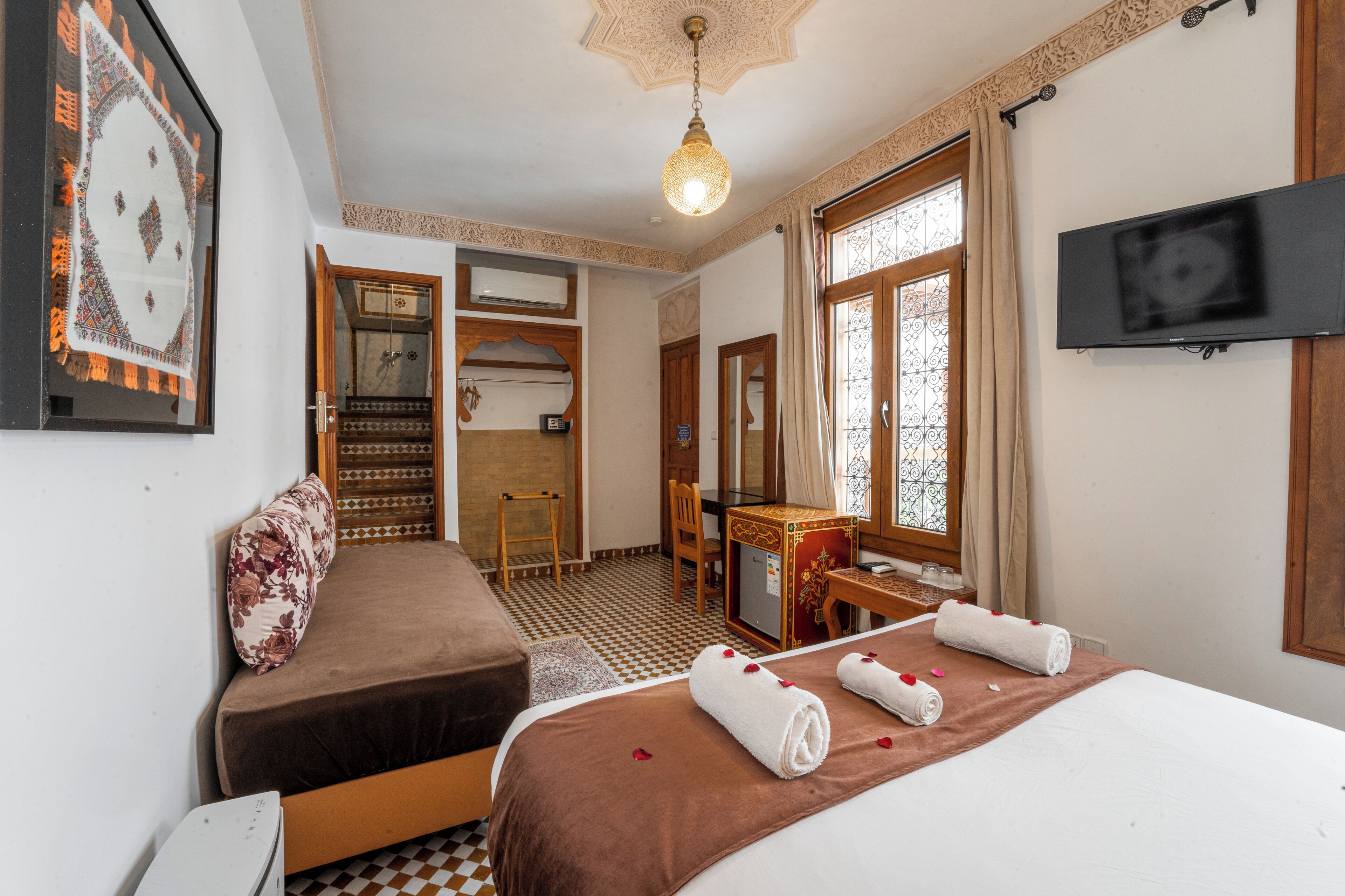 A hotel room with a bed, a desk, a chair, a TV, and a window with curtains.