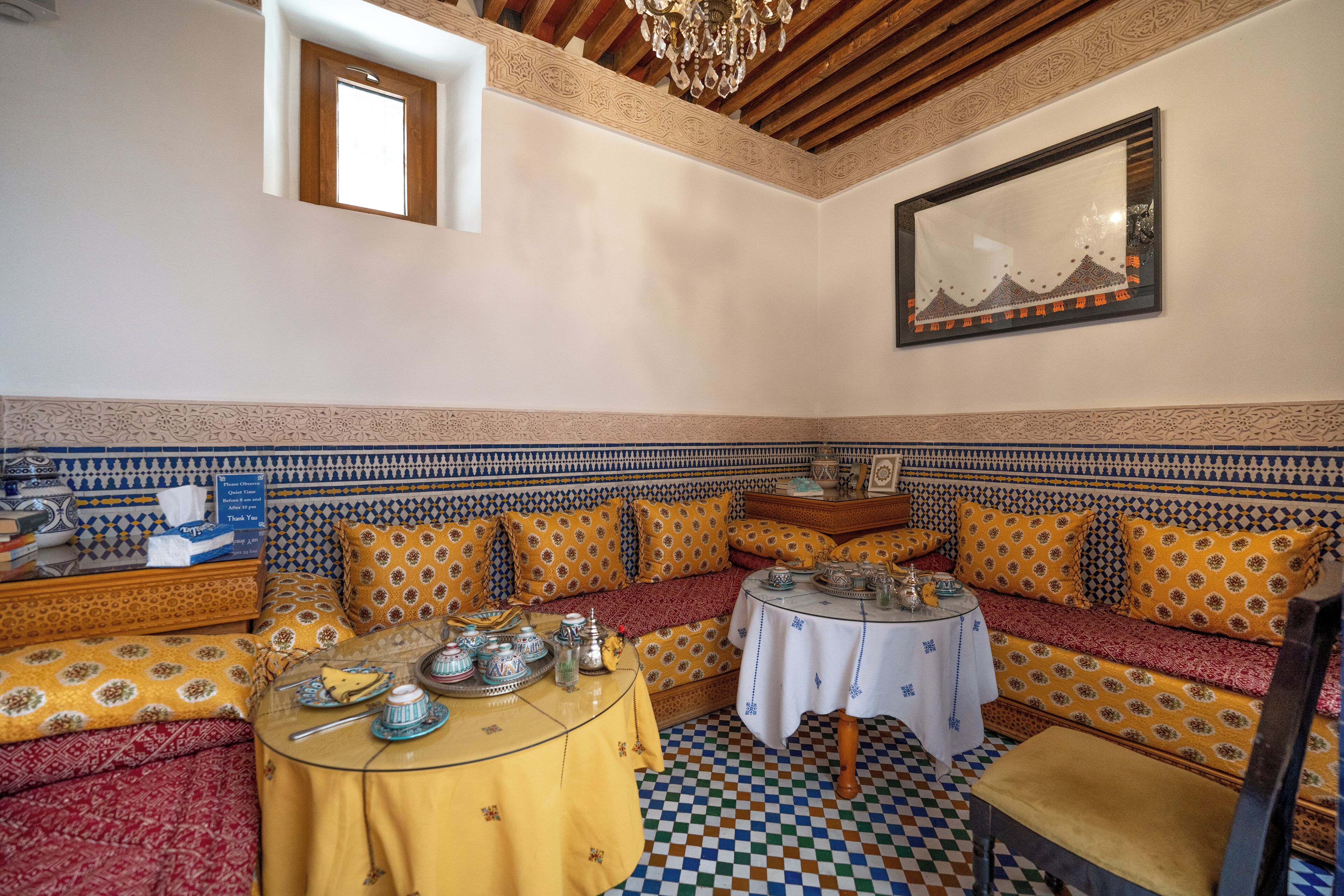 A traditional Moroccan room with patterned sofas, a small table with tea sets, and a chandelier.