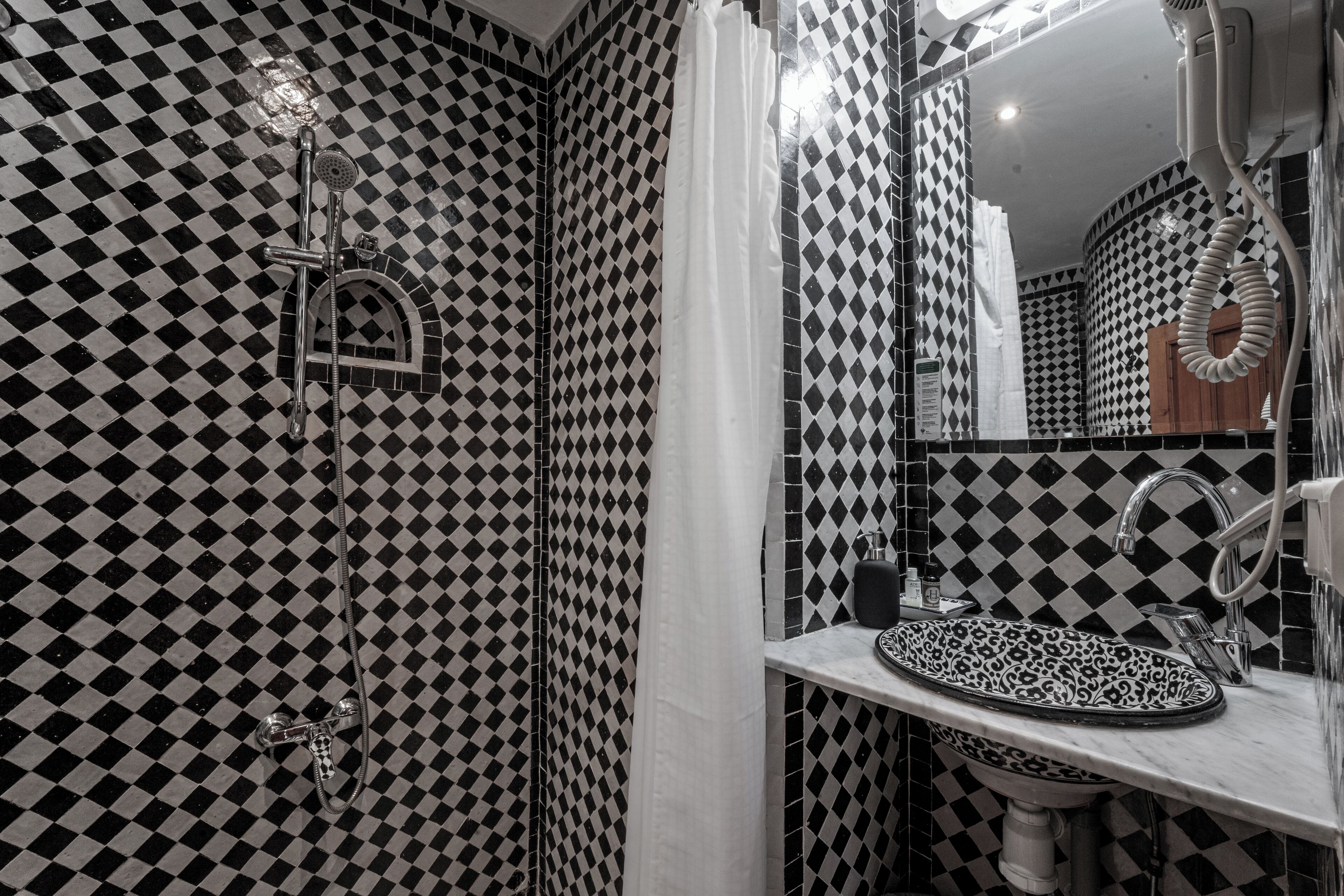 A bathroom with a checkered black and white tile pattern, a sink with a patterned basin, and a shower with a handheld showerhead.