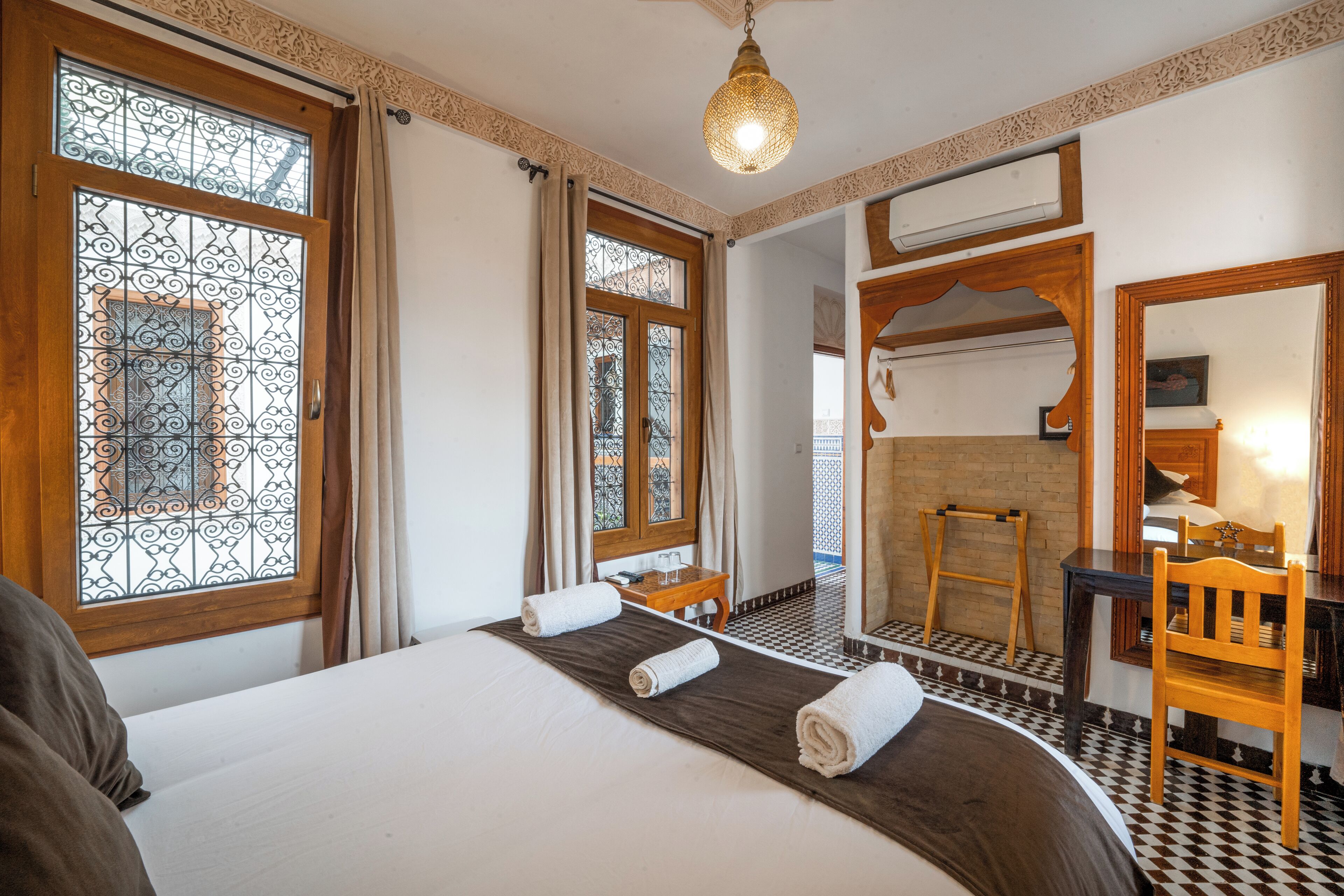 Habitación de hotel con una cama grande, un escritorio de madera, una silla, un espejo y un piso estampado.