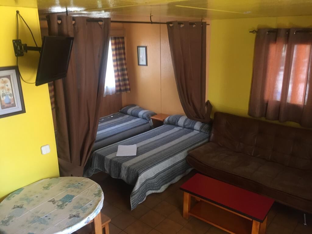 Una habitación con dos camas, un sofá, una mesita y un televisor montado en la pared.