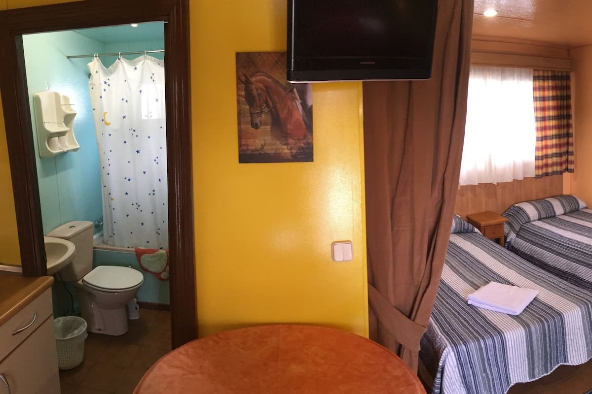 Una habitación con dos camas, televisión, ventana con cortinas, lavamanos y un inodoro.