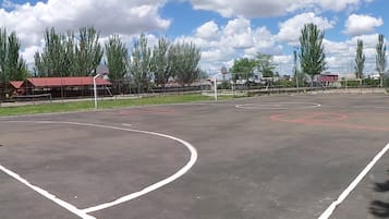 Una cancha de baloncesto al aire libre con vallas, árboles y un edificio al fondo.