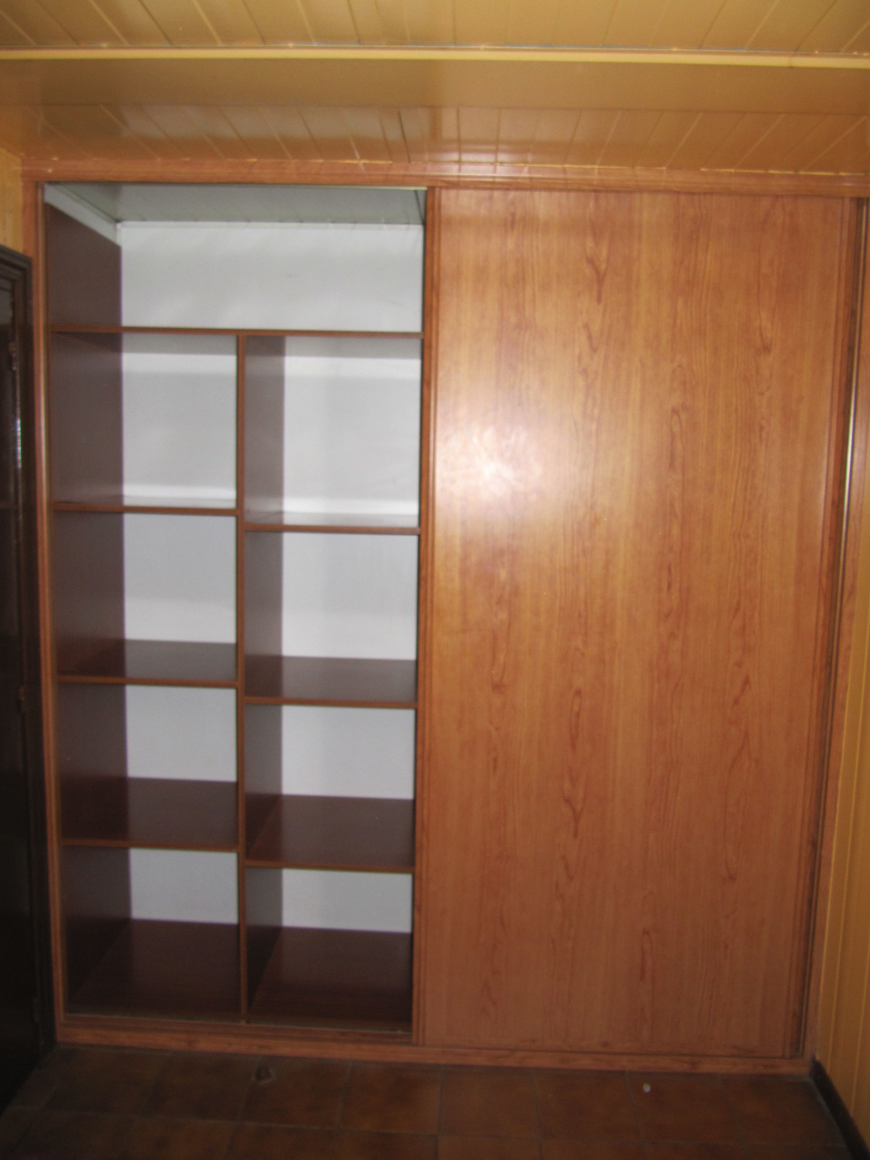 A wooden closet with multiple shelves and a sliding door.