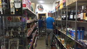 Un pasillo de tienda con estantes llenos de diversos productos, incluyendo alcohol y artículos para el hogar.