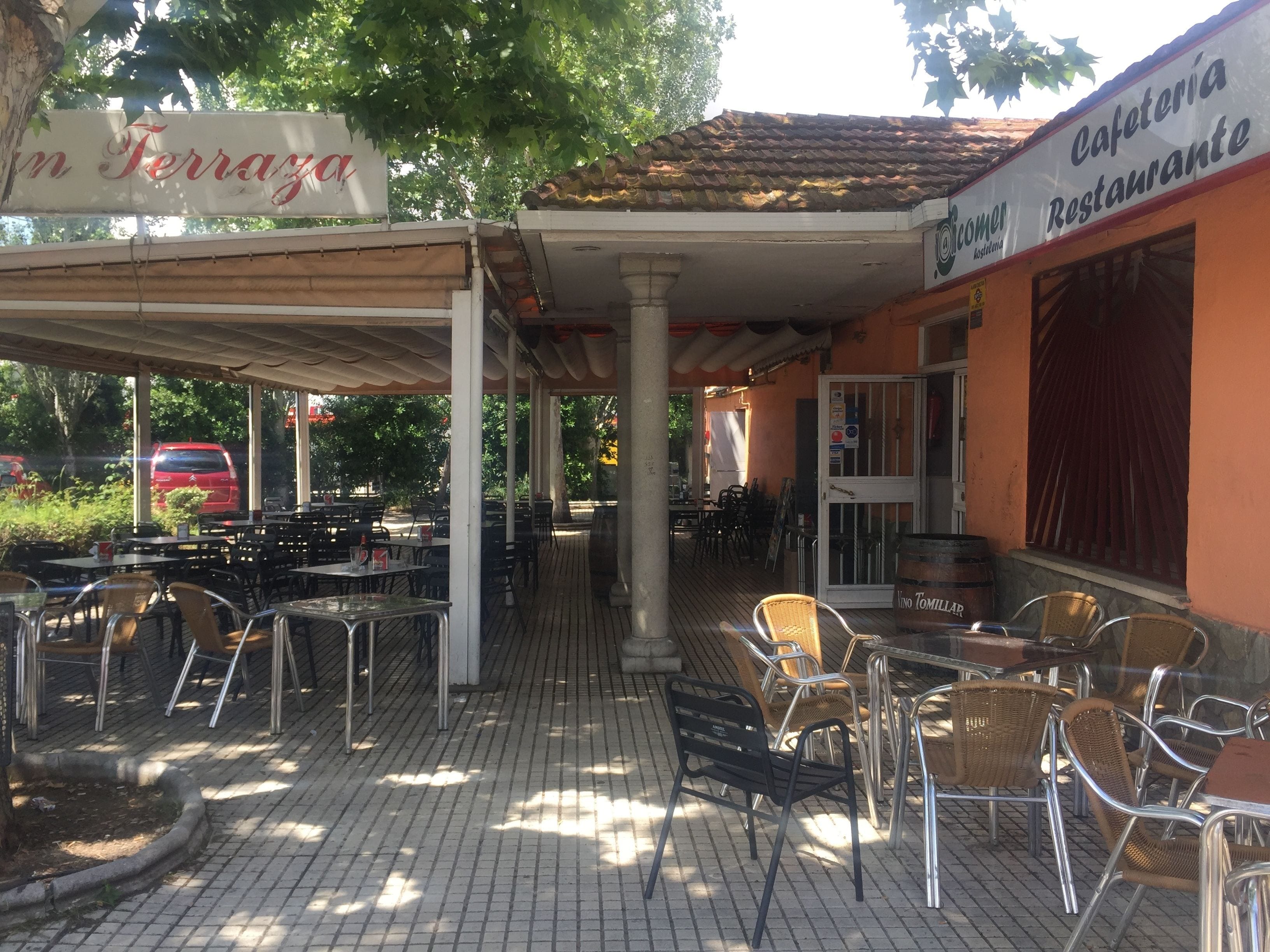 An outdoor cafe with tables and chairs, a covered seating area, and a sign for 'Cafeteria Restaurante'.