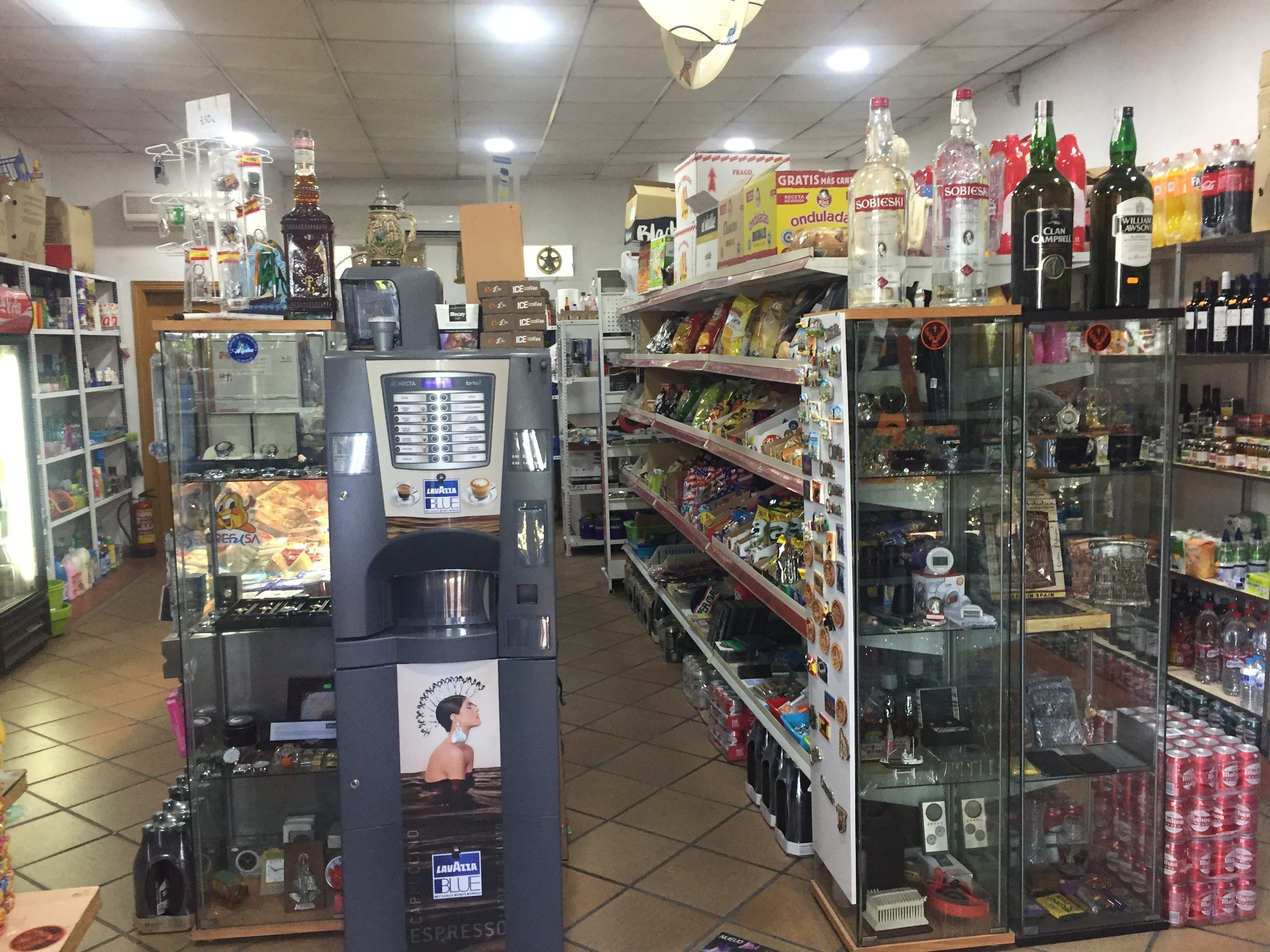 A convenience store with a coffee machine, shelves stocked with snacks, and various beverages.