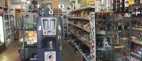A convenience store with a coffee machine, shelves stocked with snacks, and various beverages.