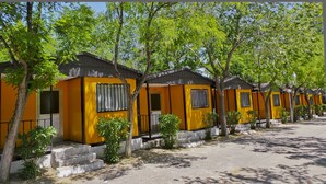 Una hilera de cabañas amarillas con techos negros, cada una con ventana y puerta, rodeadas de árboles.