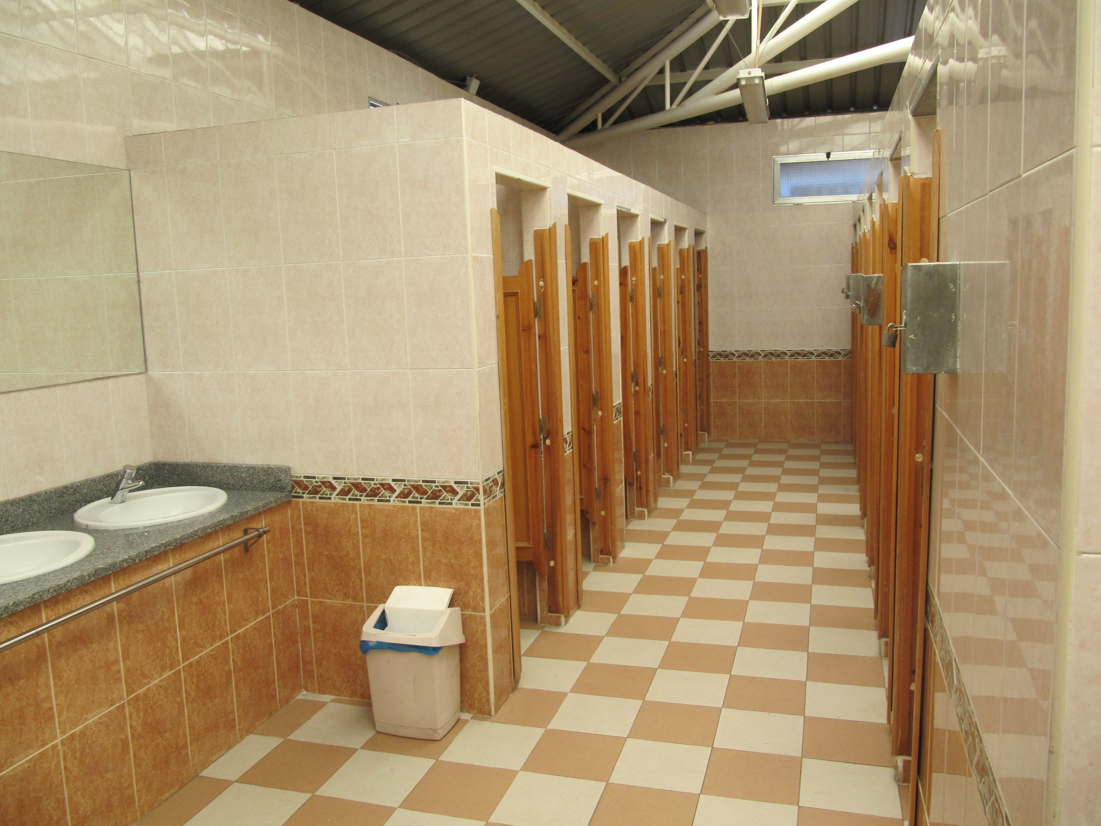 Baño público con varios lavamanos, un cesto de basura y piso de baldosas.