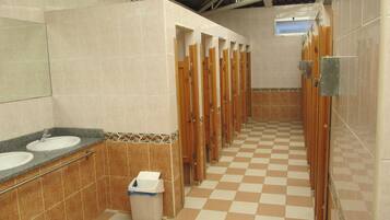 Baño público con varios lavamanos, un cesto de basura y piso de baldosas.