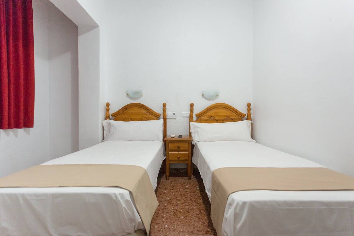 A room with two single beds, a wooden nightstand between them, and a red curtain on the left.