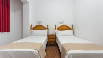 Una habitació amb dos llits individuals, una taula de nit de fusta entre ells i una cortina vermella a l'esquerra.