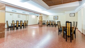 Una habitación amplia con piso pulido, techo alto con diseño tejido, y varias mesas y sillas dispuestas para comer.