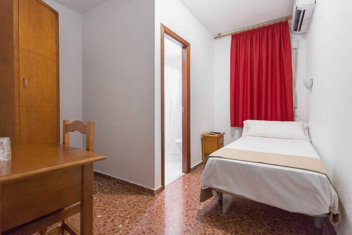 A bedroom with a bed, a wooden chair, a small table, a wardrobe, and a red curtain.