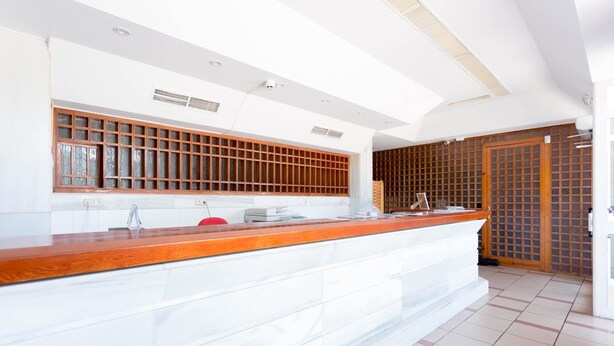 Un área de recepción con mostrador de madera, armarios blancos y suelo de baldosas.