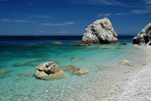 A beach with clear turquoise water, large white rocks, and a person standing near the water. - Pino bilo - One Bedroom Apartment, Sleeps 6 (Marina di Campo)