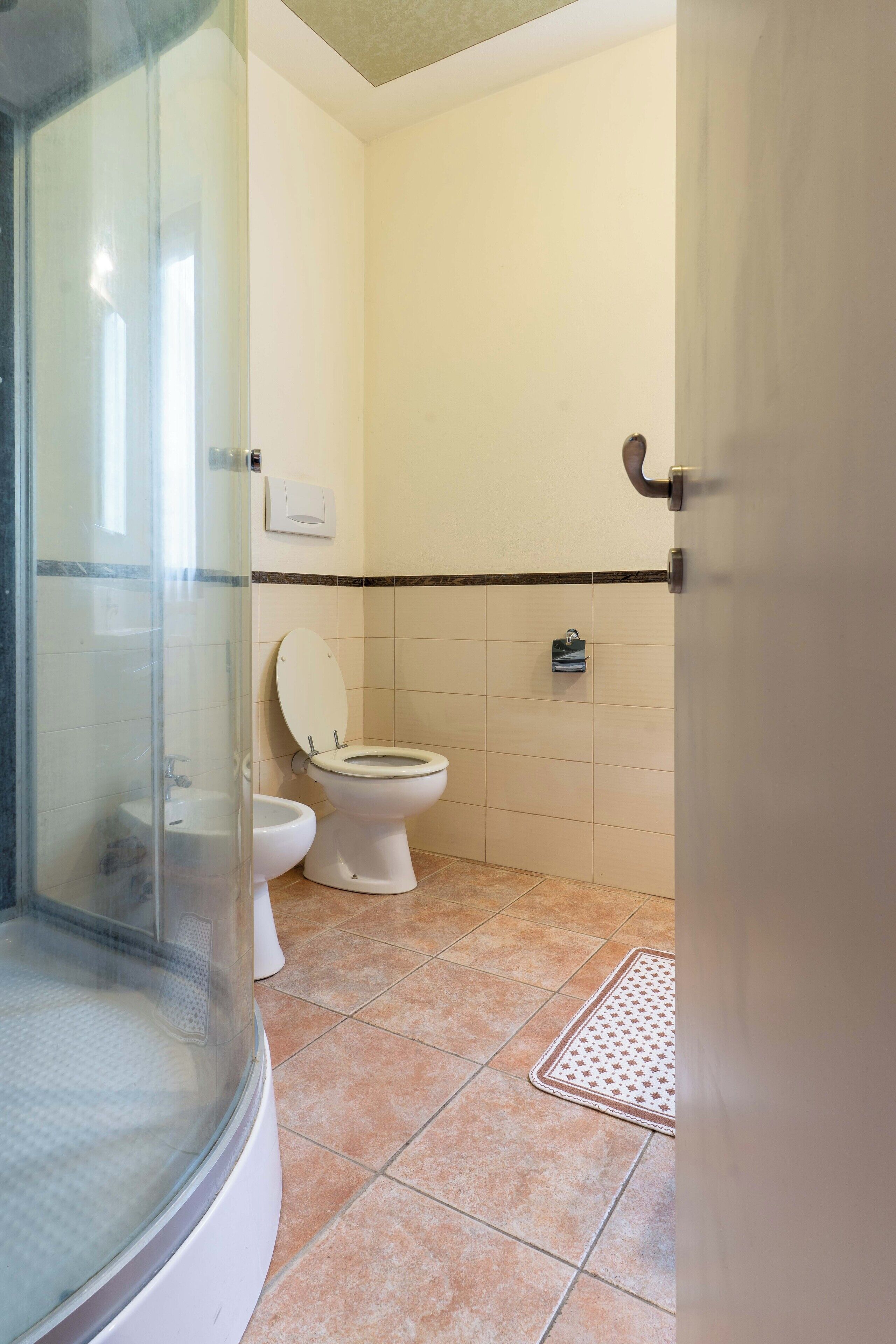 Ein Badezimmer mit Duschkabine, zwei Toiletten und Fliesenboden.