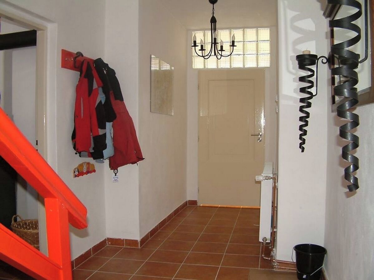 A hallway with a tiled floor, a door, and a wall-mounted coat rack with jackets.