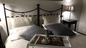 Una cama bien hecha con almohadas, una mesita de noche con cafetera, tazas y una bandeja.