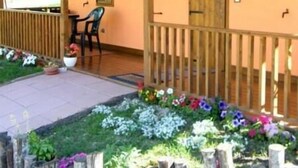 Un espacio al aire libre cubierto con una terraza de madera, cerca de madera y un parterre con diversas flores.
