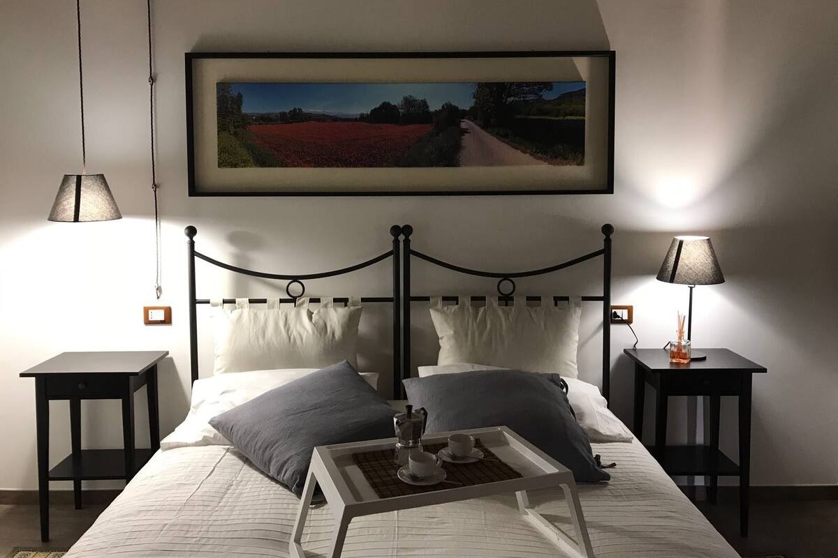 A bedroom with a bed, two bedside tables, a nightstand, a framed picture on the wall, and a lamp on each bedside table.