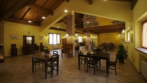 Un comedor espacioso con techos altos y vigas de madera a la vista, con varias mesas y sillas.