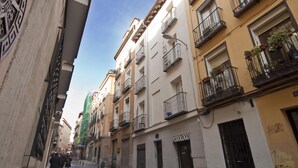 Una calle estrecha bordeada de edificios de varios pisos, algunos con balcones y plantas en macetas.