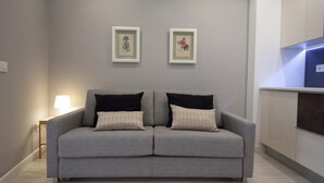 Una sala de estar moderna con un sofá gris, dos cuadros con flores en la pared y una mesita de noche con una lámpara.