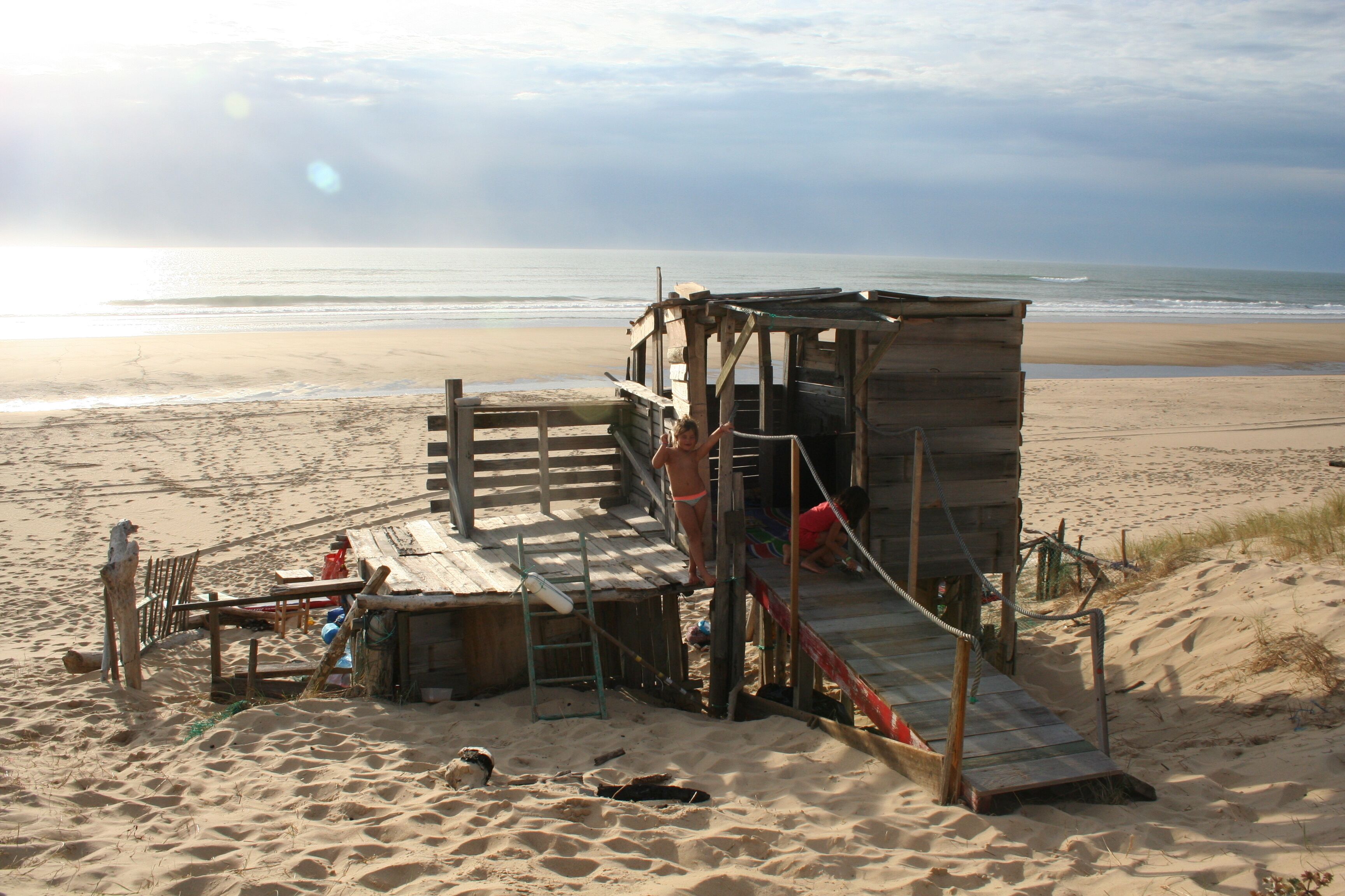A wooden beach hut with a slide, located on a sandy beach with the ocean in the background.