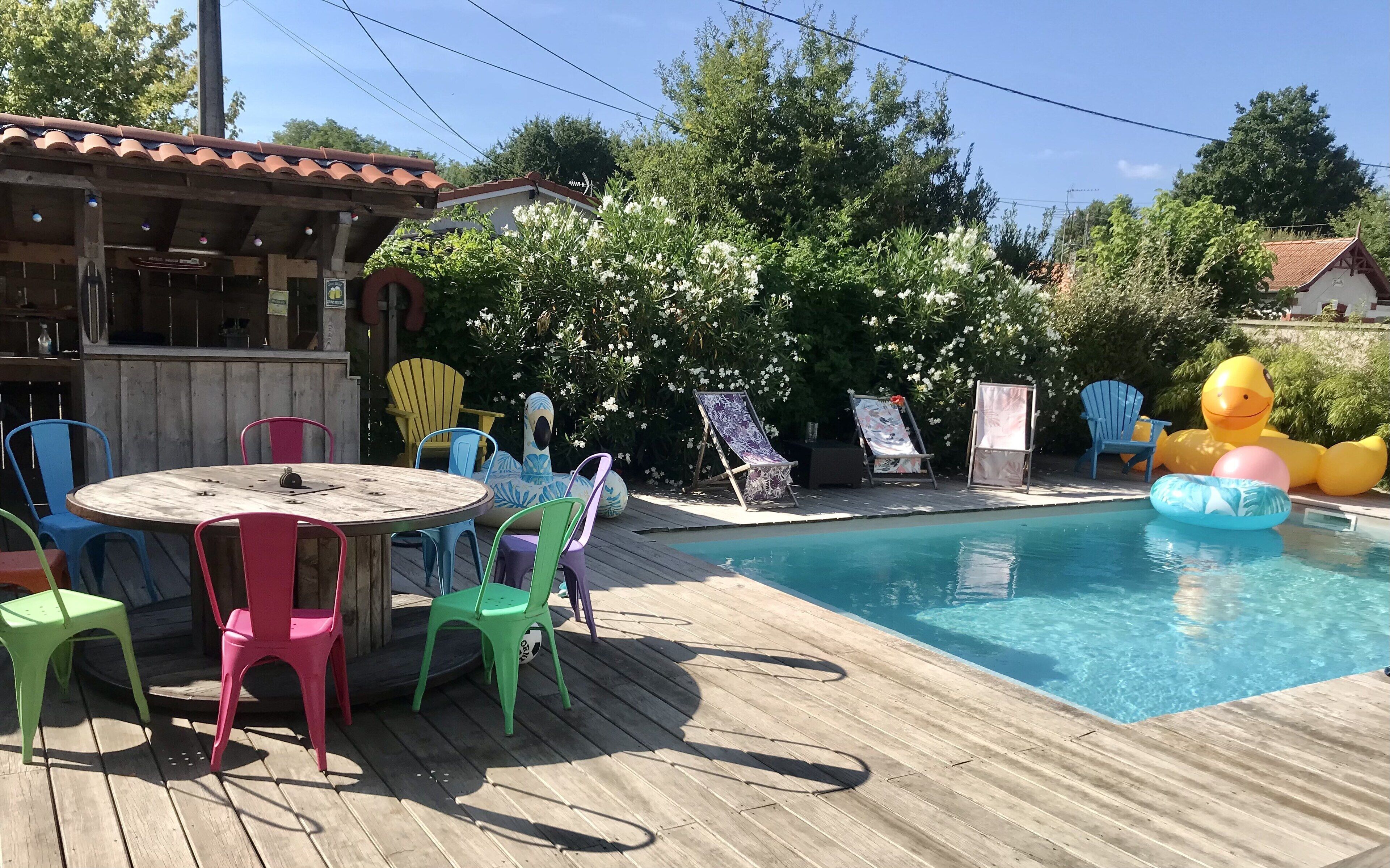A wooden deck with a pool, surrounded by colorful chairs and a dining table.