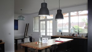 Una cocina moderna con una mesa de madera, sillas negras y lámparas colgantes.