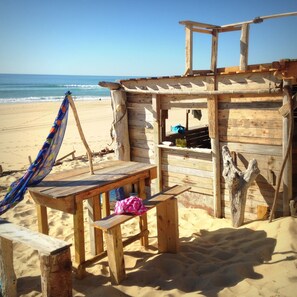 Een houten strandhut met een bankje en een hangmat, met uitzicht op de oceaan.