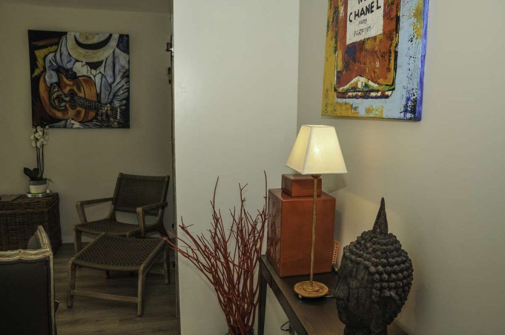 Uma sala de estar com uma luminária, cadeiras, um quadro de guitarra e um anúncio de perfume na parede.