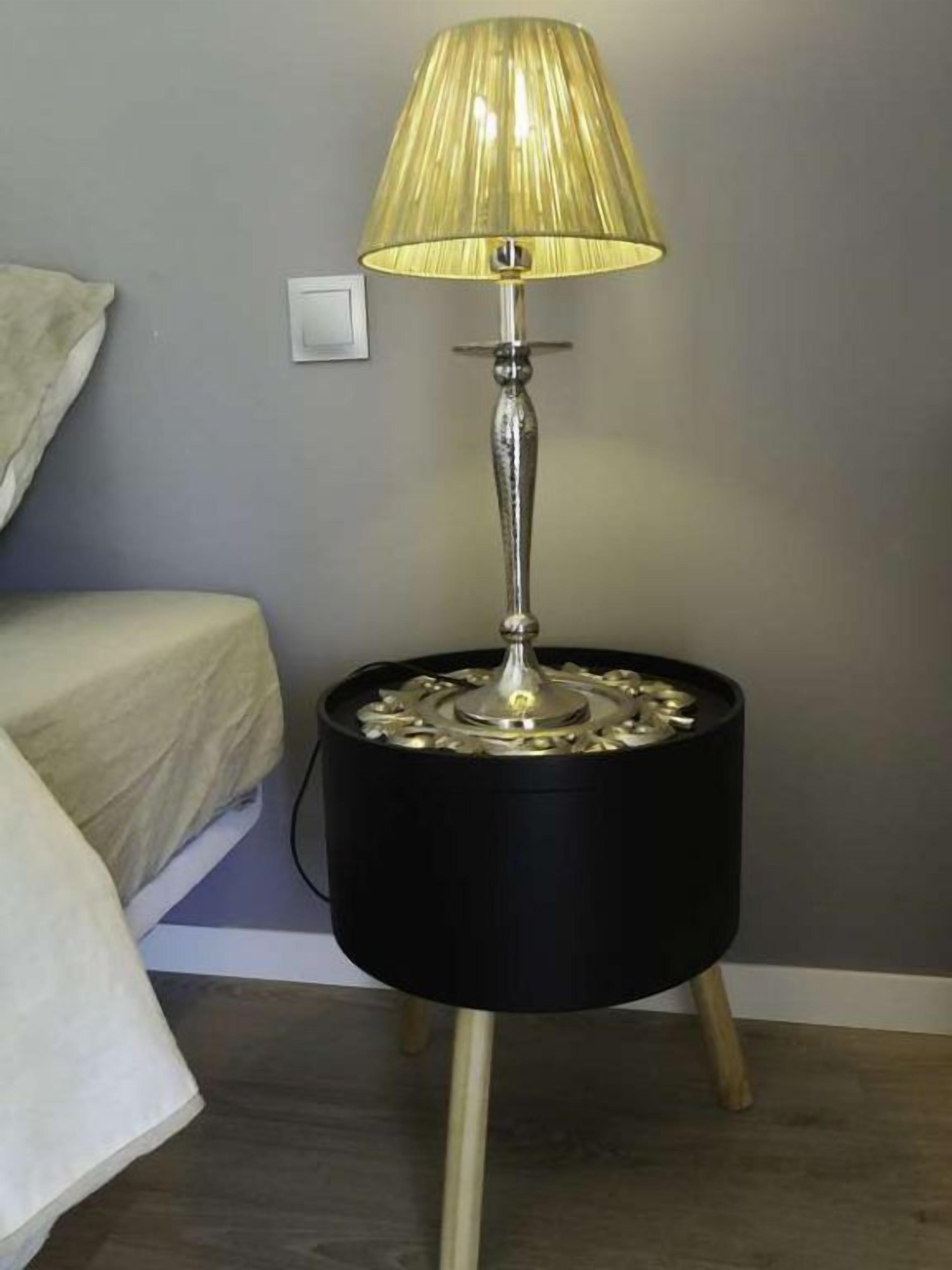 A lamp with a black base and a metallic stand, placed on a wooden floor.