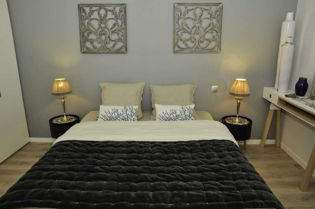 Un dormitorio con una cama, dos lámparas de noche, una mesita de noche, una pequeña mesa y decoración en la pared.