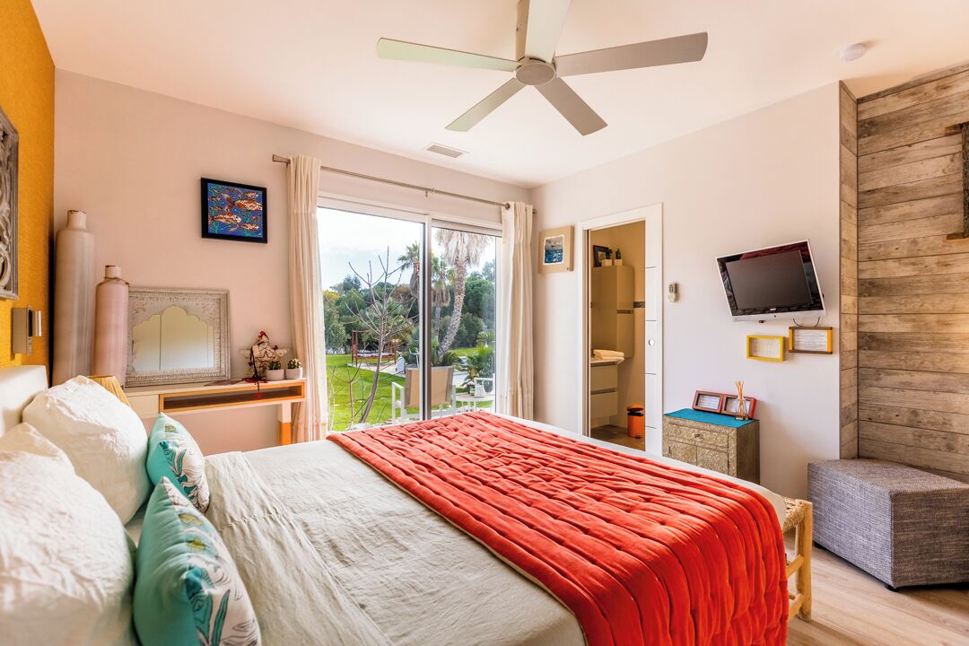 A bedroom with a bed, a ceiling fan, a TV, and a view of the outdoors.
