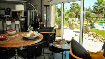 A modern kitchen with a dining area, large windows, and a view of a pool and garden.