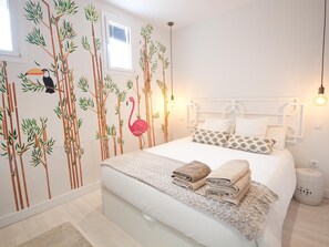 Une chambre à coucher avec un lit, des oreillers et une fresque murale représentant un toucan et un flamant rose.