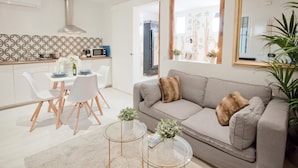 A modern living room with a grey sofa, a coffee table, and a dining area with white chairs and a small table. - A perfect refuge in Madrid's city center (Madrid)