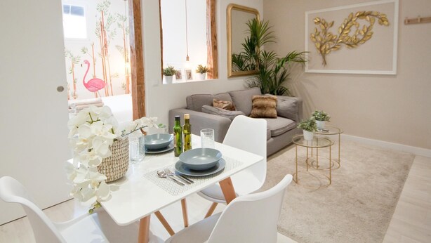 A dining area with a white table set for four, a grey sofa, and a small round side table with a plant. - A perfect refuge in Madrid's city center (Madrid)