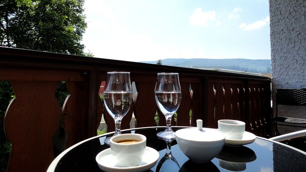 A table with a cup of coffee, a glass of water, and a wine glass, with a view of the mountains in the background.