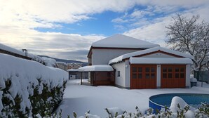 A snow-covered house with a garage, a covered patio, and a swimming pool.