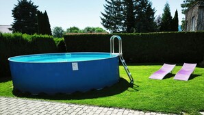 An above-ground swimming pool with a ladder, surrounded by a well-maintained lawn and a paved walkway.