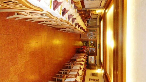 A long corridor with rows of tables and chairs, leading to a bar area with a counter and stools. - Albergo Ristorante Fratte (Fregona)