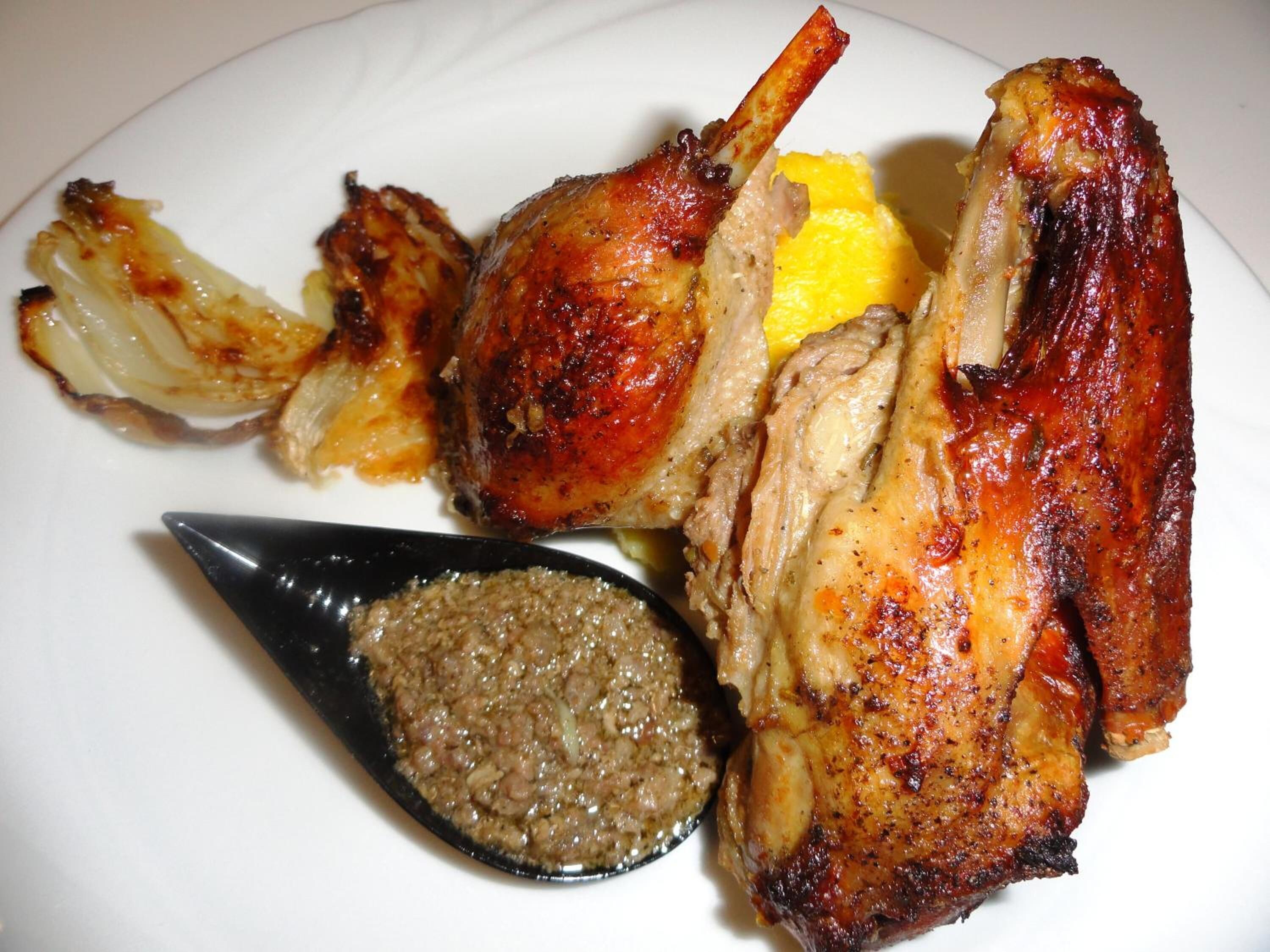 A plate with roasted chicken, lemon slices, and a sauce.