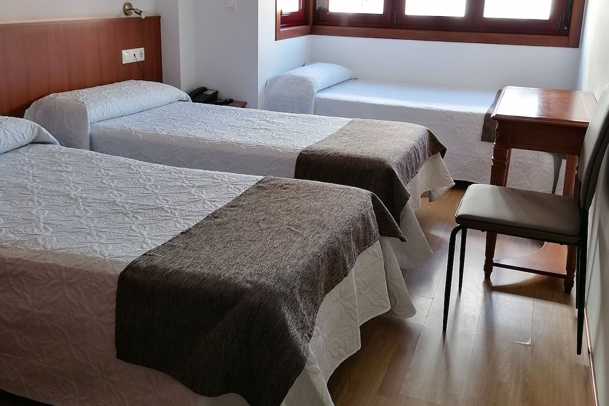 A hotel room with two single beds, a wooden desk, a chair, and a window with blinds.