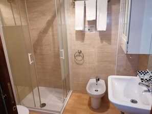 A bathroom with a glass-enclosed shower, a pedestal sink, and a bidet. - Hostal Adelia (A Coruña)