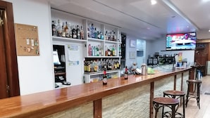 A bar area with a long counter, stools, and shelves stocked with various bottles. - Hostal Adelia (A Coruña)