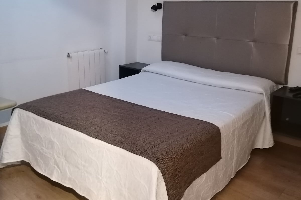 A bedroom with a bed, a nightstand, a wall-mounted lamp, and a painting.